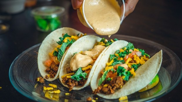 Person pouring out sauce on tacos