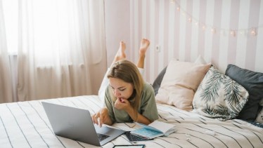Woman lying on bed while working on her laptop